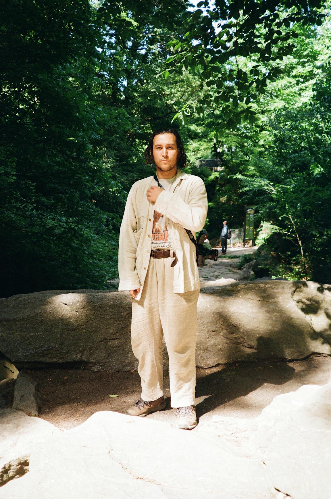 A portrait photo of a masculine person in a lush park.